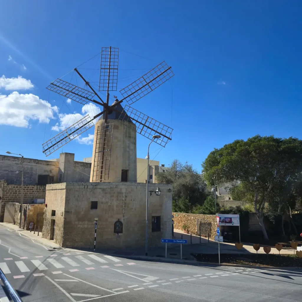 O moară de vânt istorică din piatră, Ta' Kola Windmill, în Xagħra, Gozo, Malta, sub un cer albastru cu nori albi.